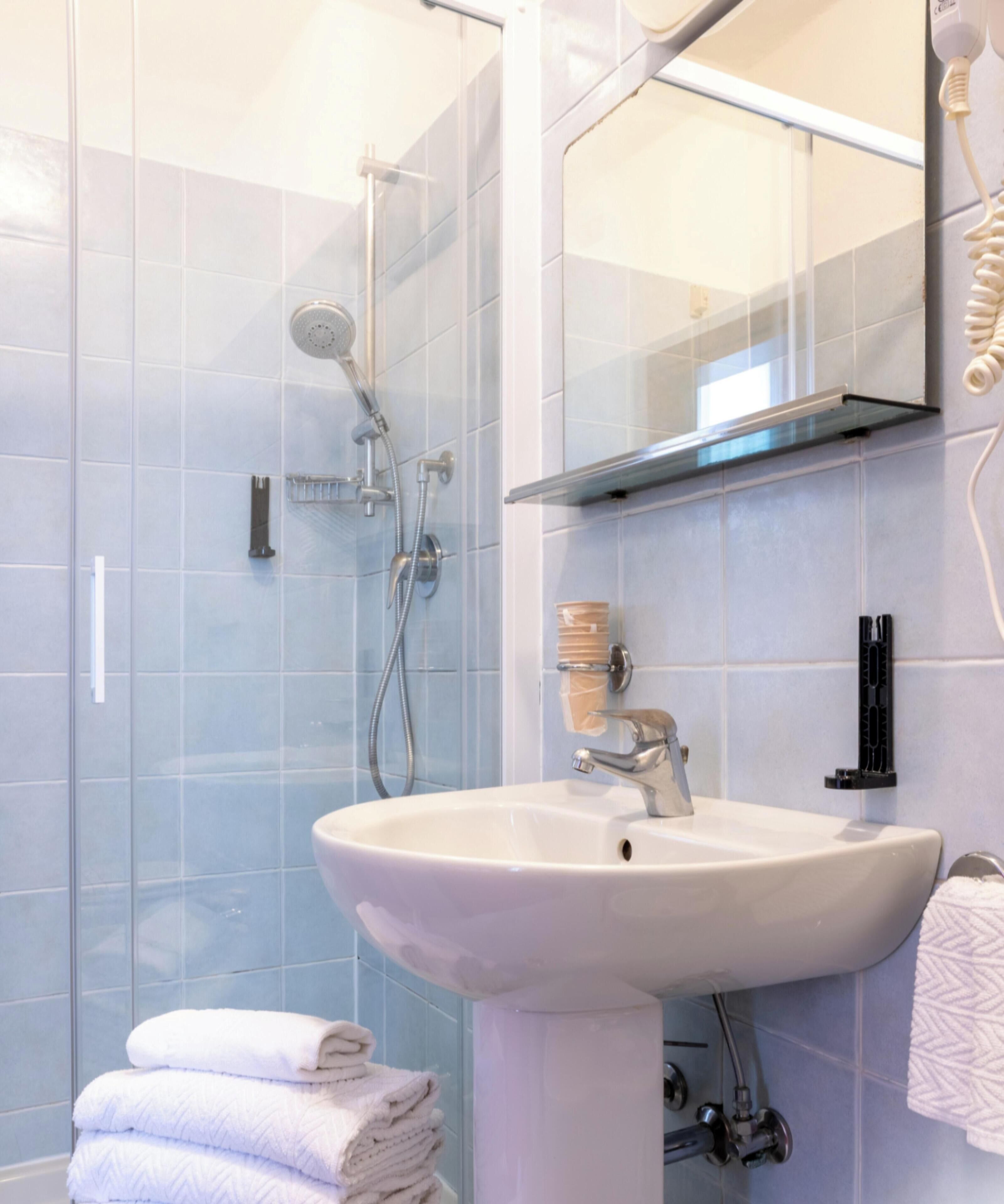 Ein Badezimmer mit Glasdusche, einem weißen Waschbecken und einem Handtuchhalter mit gefalteten Handtüchern.