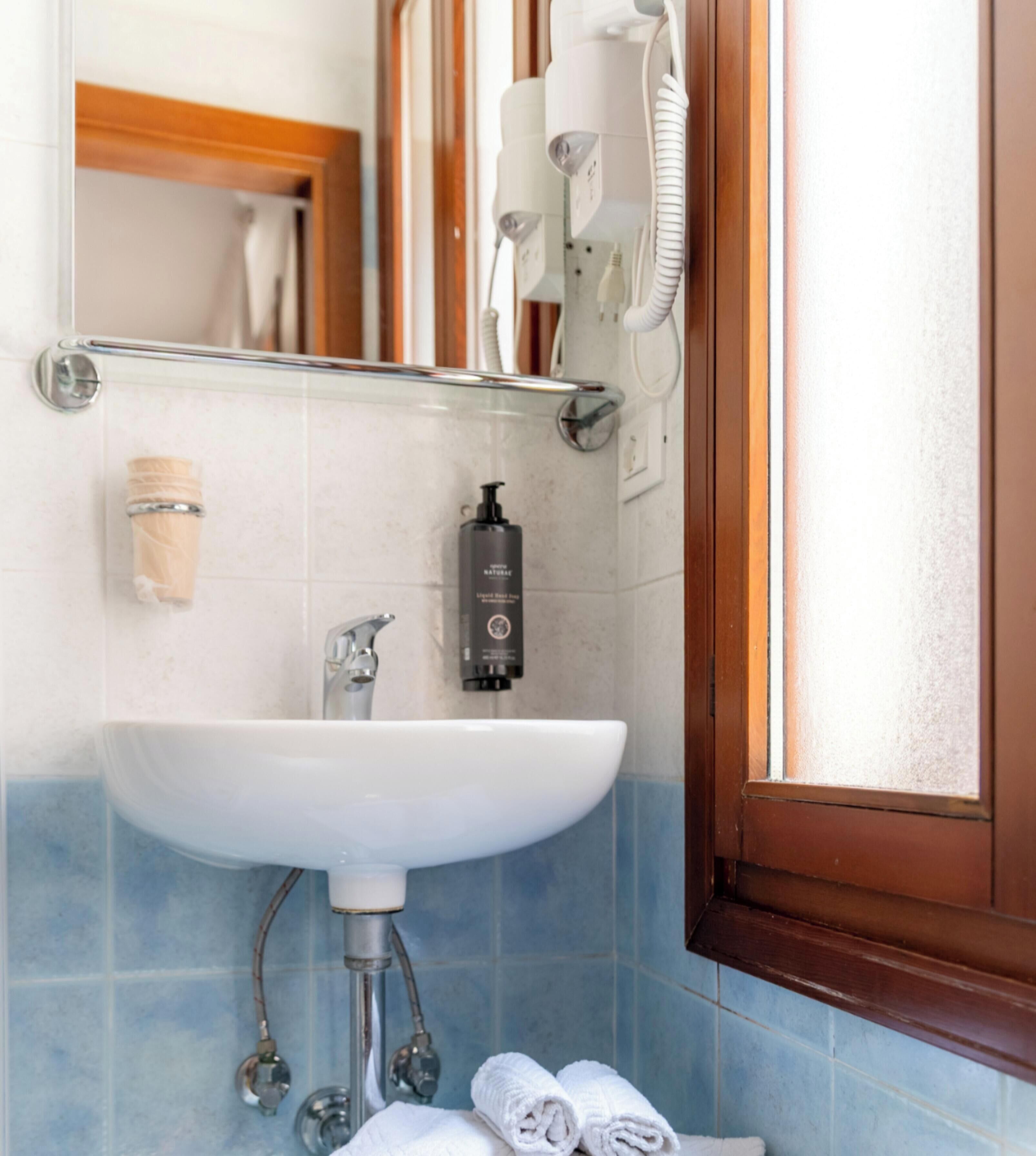 A bathroom with a white sink, a mirror, a hairdryer, and a bottle of liquid soap.