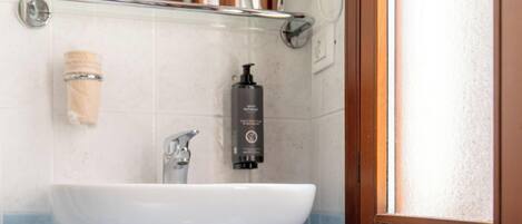 A bathroom with a white sink, a mirror, a hairdryer, and a bottle of liquid soap.