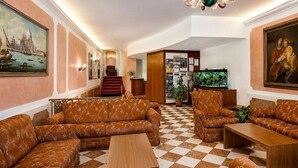 Un vestíbulo de hotel con piso a cuadros, sofás, una mesa de centro de madera, un candelabro, una escalera y obras de arte en las paredes.