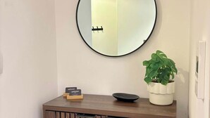 Una consola de madera con un espejo redondo, una pequeña planta en maceta y un tazón negro encima.