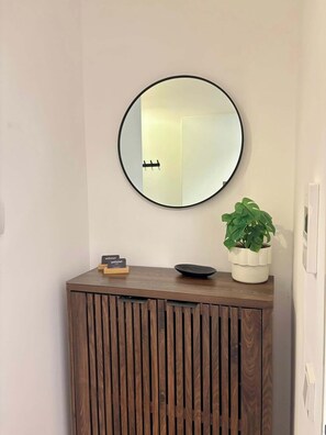 Una consola de madera con un espejo redondo, una pequeña planta en maceta y un tazón negro encima.