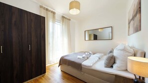 Un dormitorio con un armario amplio, una cama con almohadas y una colcha, una lámpara de noche y un espejo en la pared.