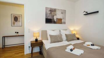 A hotel room with a bed, bedside lamps, a nightstand, a painting, and a shelf with a plant.