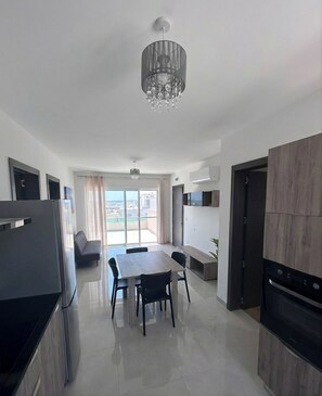 A modern kitchen with a dining area, a chandelier, and a view through the glass door. - Cittadella 2BD Penthouse, Huge Terrace With View (San Ġiljan)
