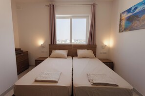 Ein Doppelzimmer mit zwei Betten, einem Fenster mit Vorhängen, Nachttischlampen und einem Bild an der Wand.