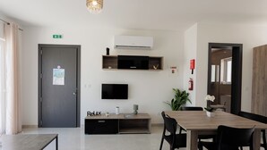 Habitació d'hotel moderna amb taula de dinar de fusta, cadires negres, televisió de pantalla plana, una petita planta i un cartell a la paret que diu 'Relax'.