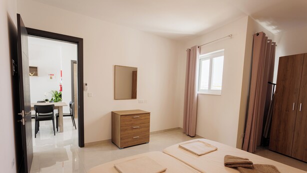 Habitació d'hotel amb un llit, escriptori, cadira, armari i un bany visible a través d'una porta oberta.