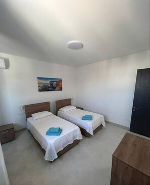 A room with two beds, a painting on the wall, and a door. - Cittadella 2BD Penthouse, Huge Terrace With View (San Ġiljan)