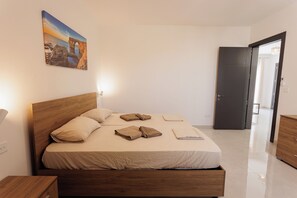 Une chambre à coucher avec un lit en bois, du linge de lit blanc et un tableau représentant un paysage côtier.