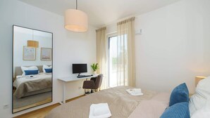 A hotel room with a bed, a desk with a computer, a chair, a large mirror, and a window with curtains.