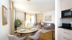 A modern living space with a dining area, a sofa, a kitchen with a black microwave, and a large window.