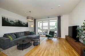 Ein modernes Wohnzimmer mit einem Ecksofa, zwei runden Tischen, einem Flachbildfernseher und einem großen Fenster mit Vorhängen.