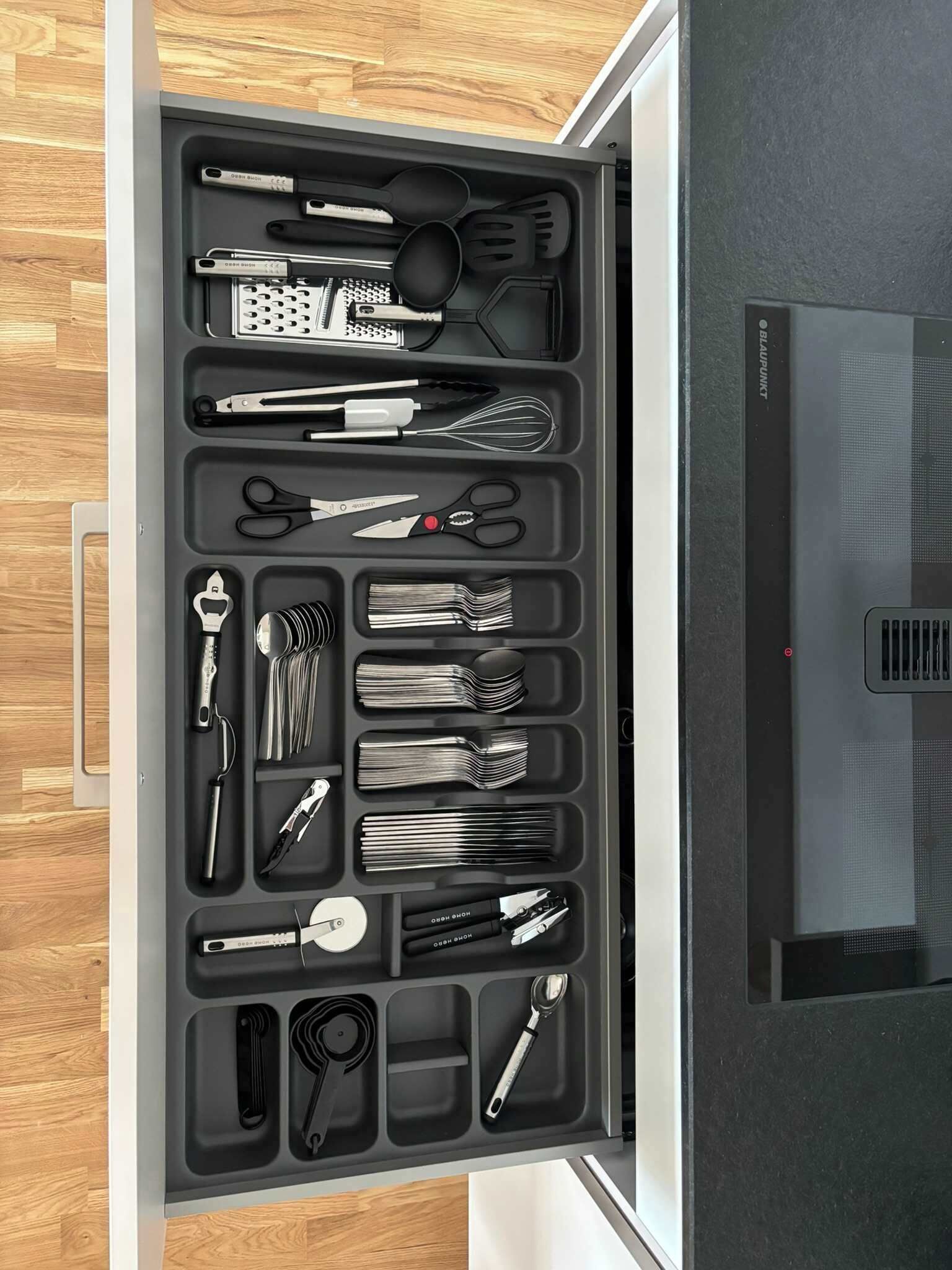 Uma gaveta com utensílios e ferramentas de cozinha, organizados em divisórias.