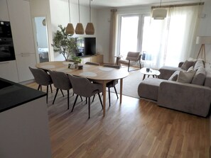 Ein modernes Wohnzimmer mit einer Couch, einem Esstisch mit Stühlen und einer Küchenzeile mit Schränken und einem Fernseher.