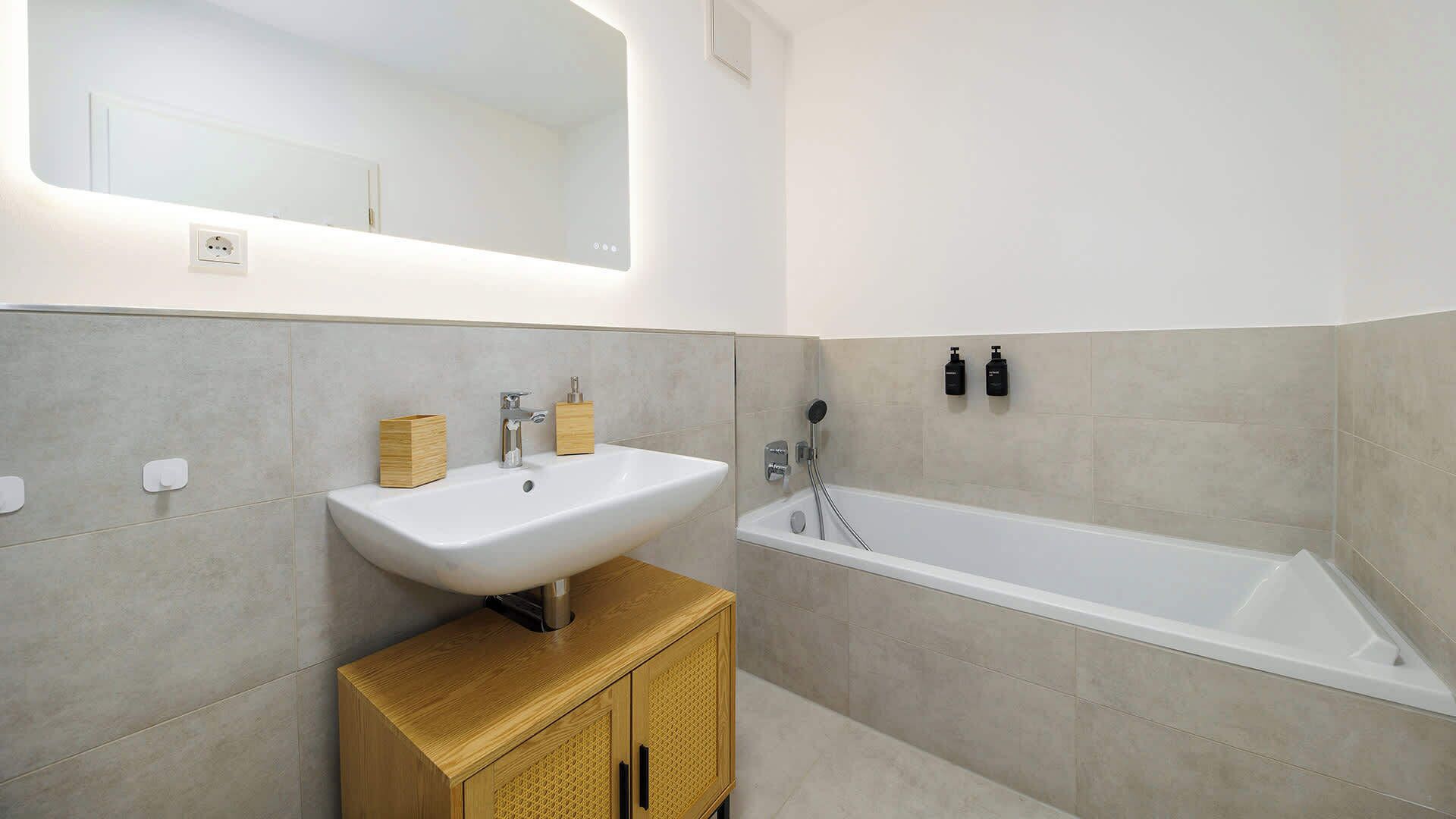 Ein modernes Badezimmer mit einem weißen Waschbecken, einem Holfach und einer Badewanne.