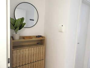 Ein Badezimmer mit einem Holzbadezimmer, einem runden Spiegel, einer Topfpflanze und einem 'HelloStay'-Schild.