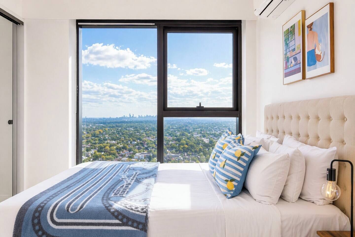 A bedroom with a large window, a bed with patterned bedding, and a city view.