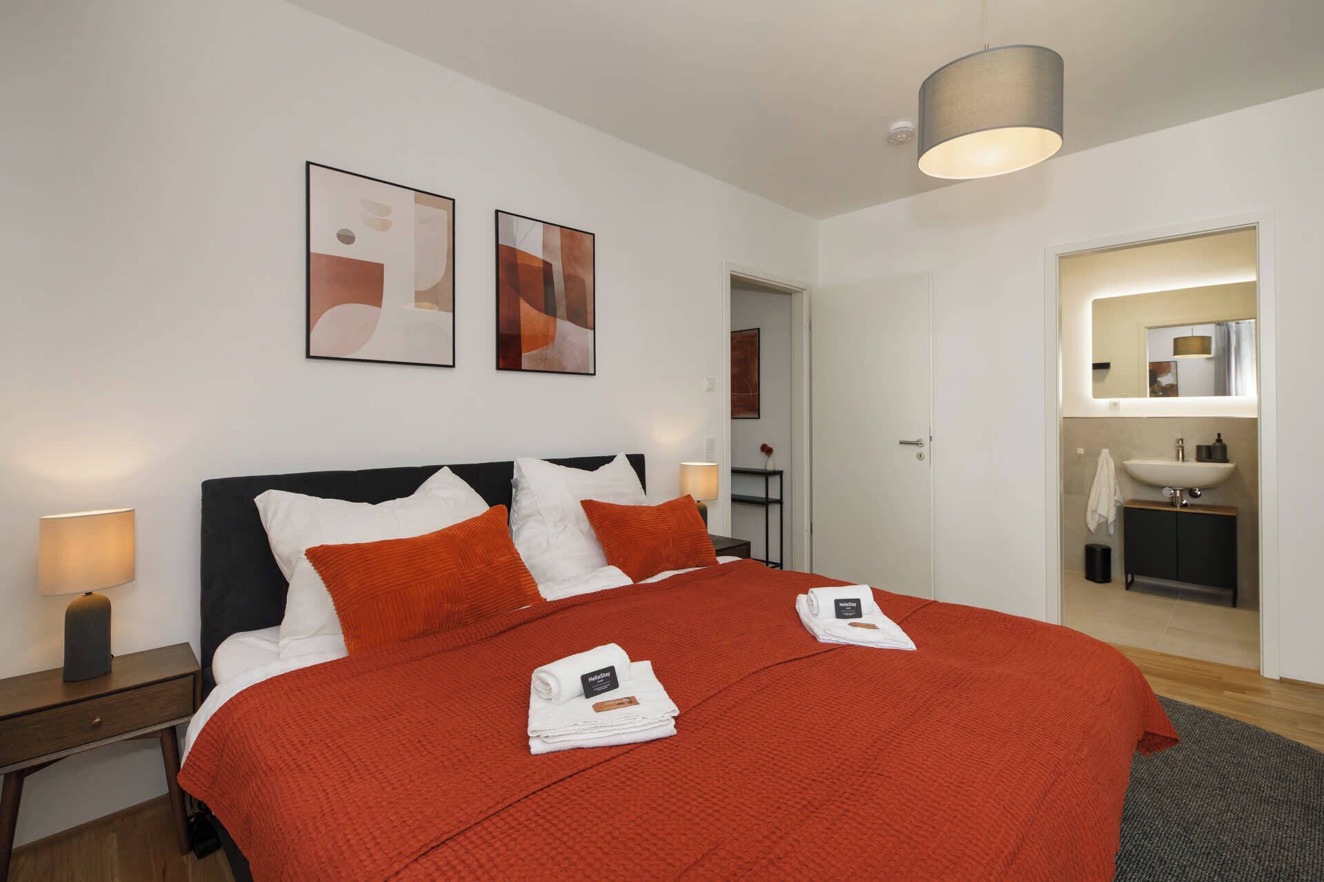 A hotel room with a large bed, two bedside lamps, a door leading to a bathroom, and two framed pictures on the wall.