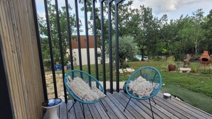 A wooden deck with two blue chairs and a white vase.