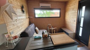 A compact kitchen with a sink, a window, and a small stool.