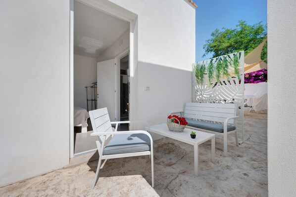 A patio with white furniture, a small table, and a basket of flowers.