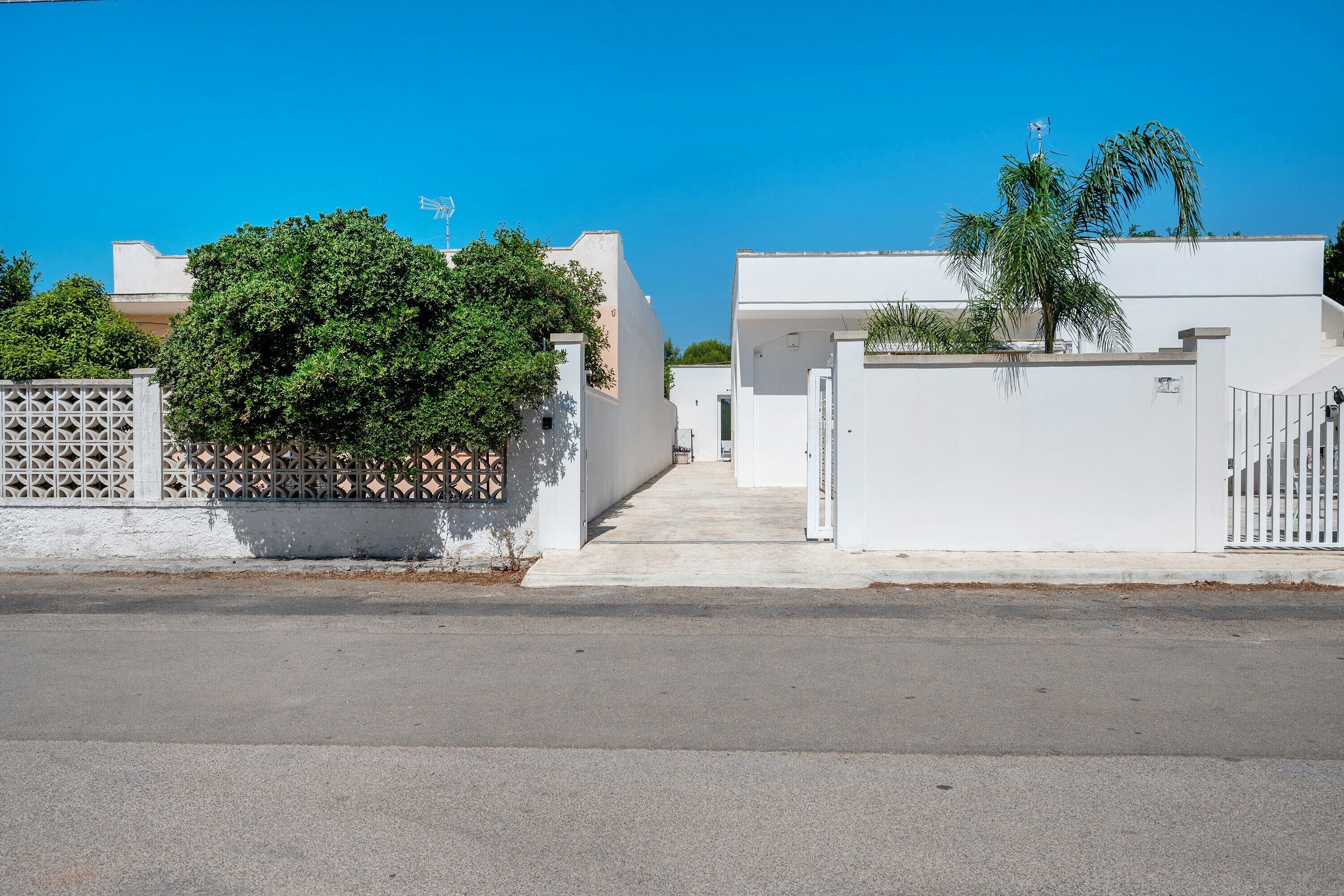 Una calle residencial con casas blancas, un acceso con reja y cielo despejado.