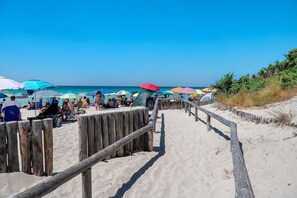 A wooden boardwalk leading to a beach with colorful umbrellas and people.