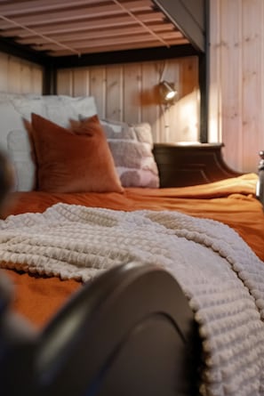 A bed with a white quilt and orange bedding, a wooden headboard, and a bedside lamp.