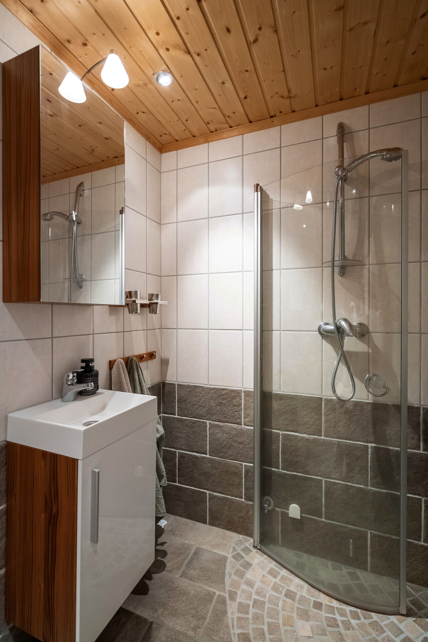 A modern bathroom with a wooden ceiling, a glass shower enclosure, a white sink, and a mirror.