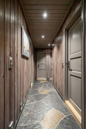 A hallway with wooden paneling, a tiled floor, and doors leading to rooms.