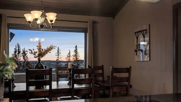 A dining area with a view of trees and a sunset, a chandelier, and a painting on the wall.