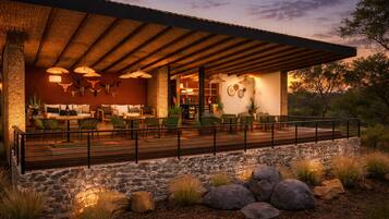 A covered outdoor seating area with stone walls and a wooden deck, furnished with chairs and tables.