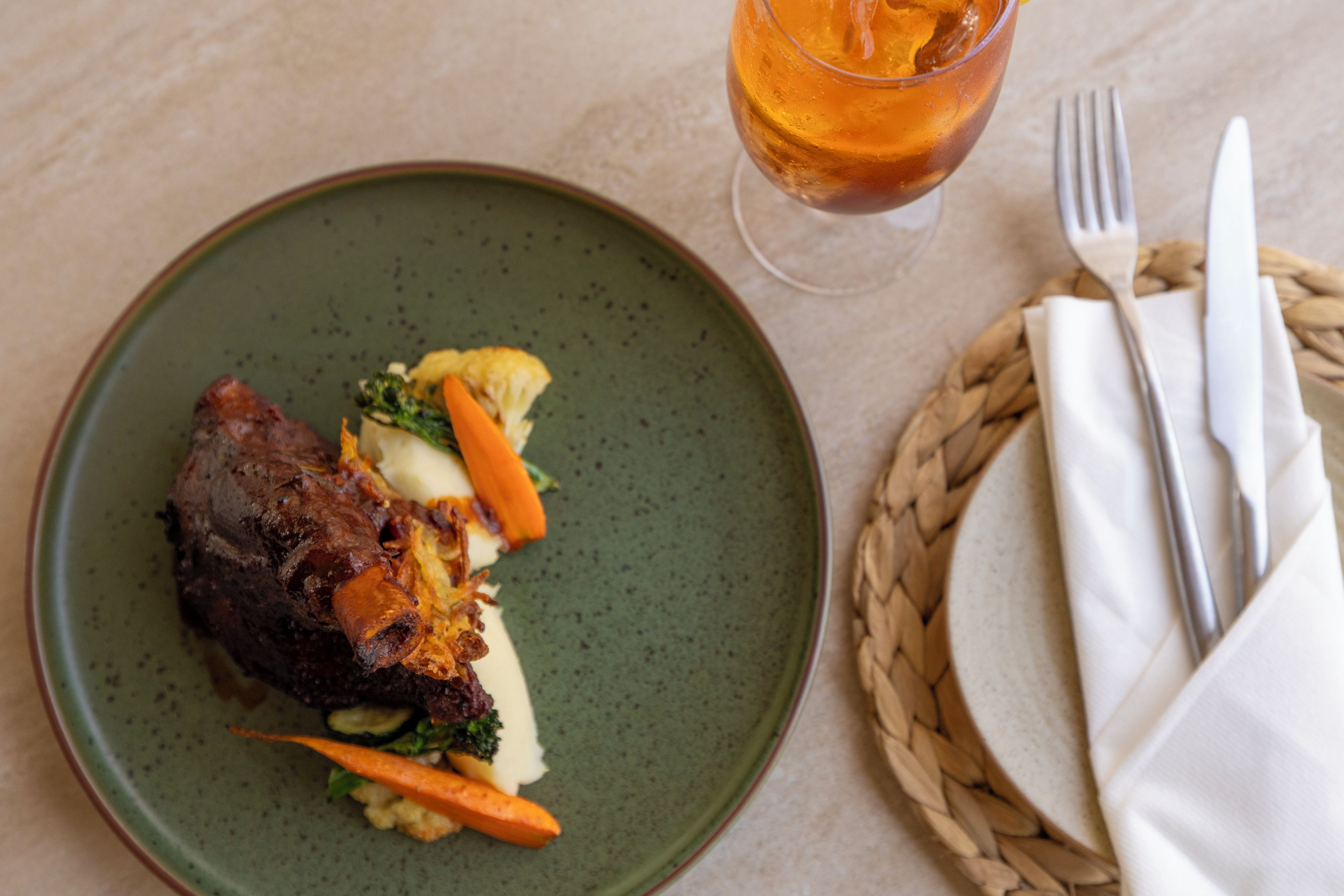 Un piatto con carne, verdure e un bicchiere di bevanda ambrata.