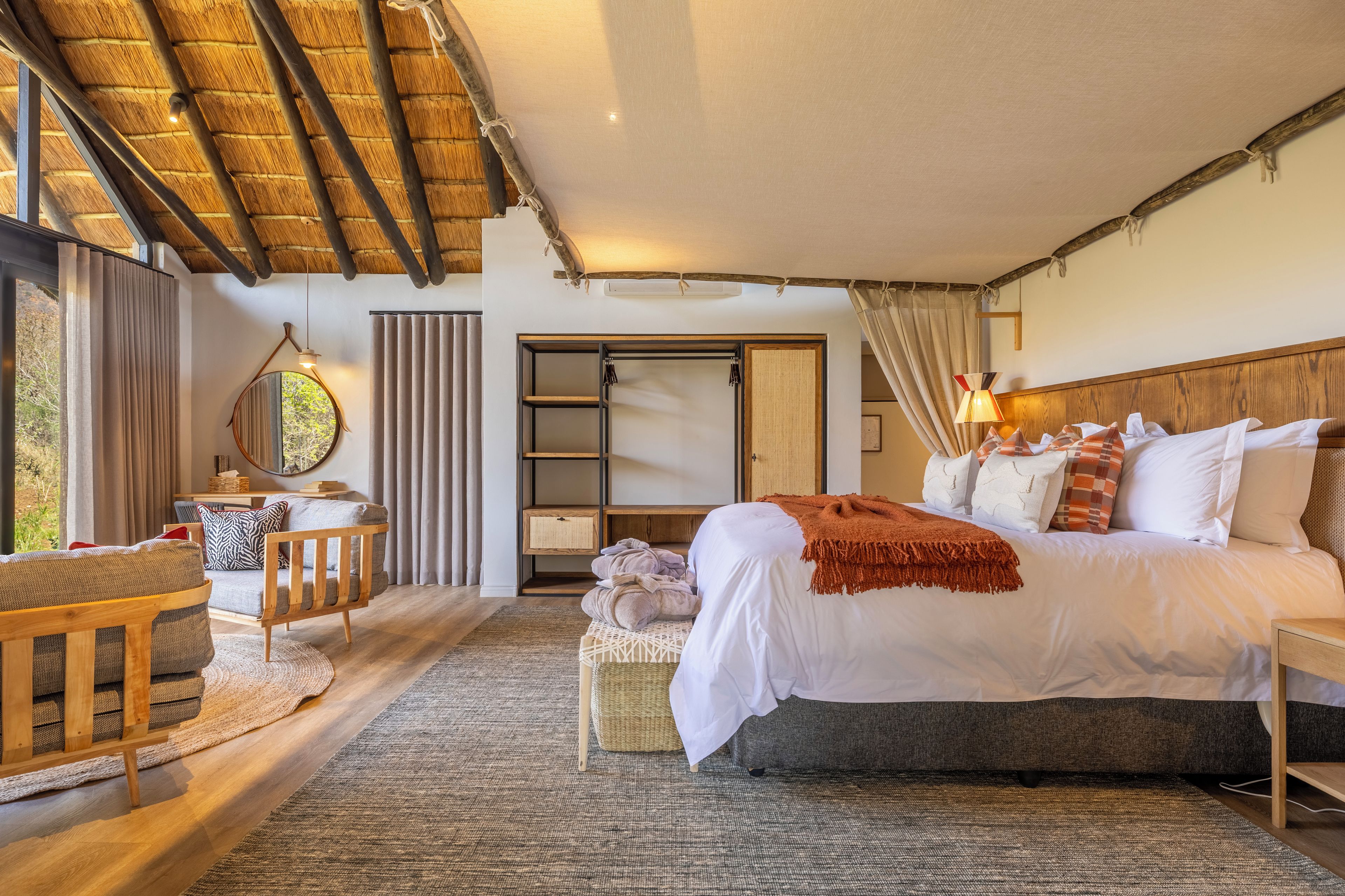 A spacious bedroom with a large bed, a wooden chair, a small table, and a view of the outdoors.