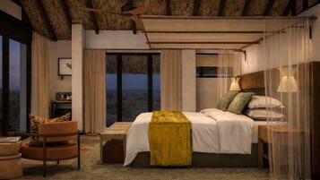 Un dormitorio con cama, una silla, mesita de noche, lámpara y vistas al exterior.