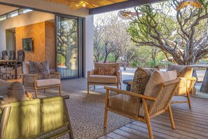 A modern outdoor seating area with wicker furniture and a view of a tree-lined landscape. - Tsholo Safari Lodge (Pilanesberg National Park)