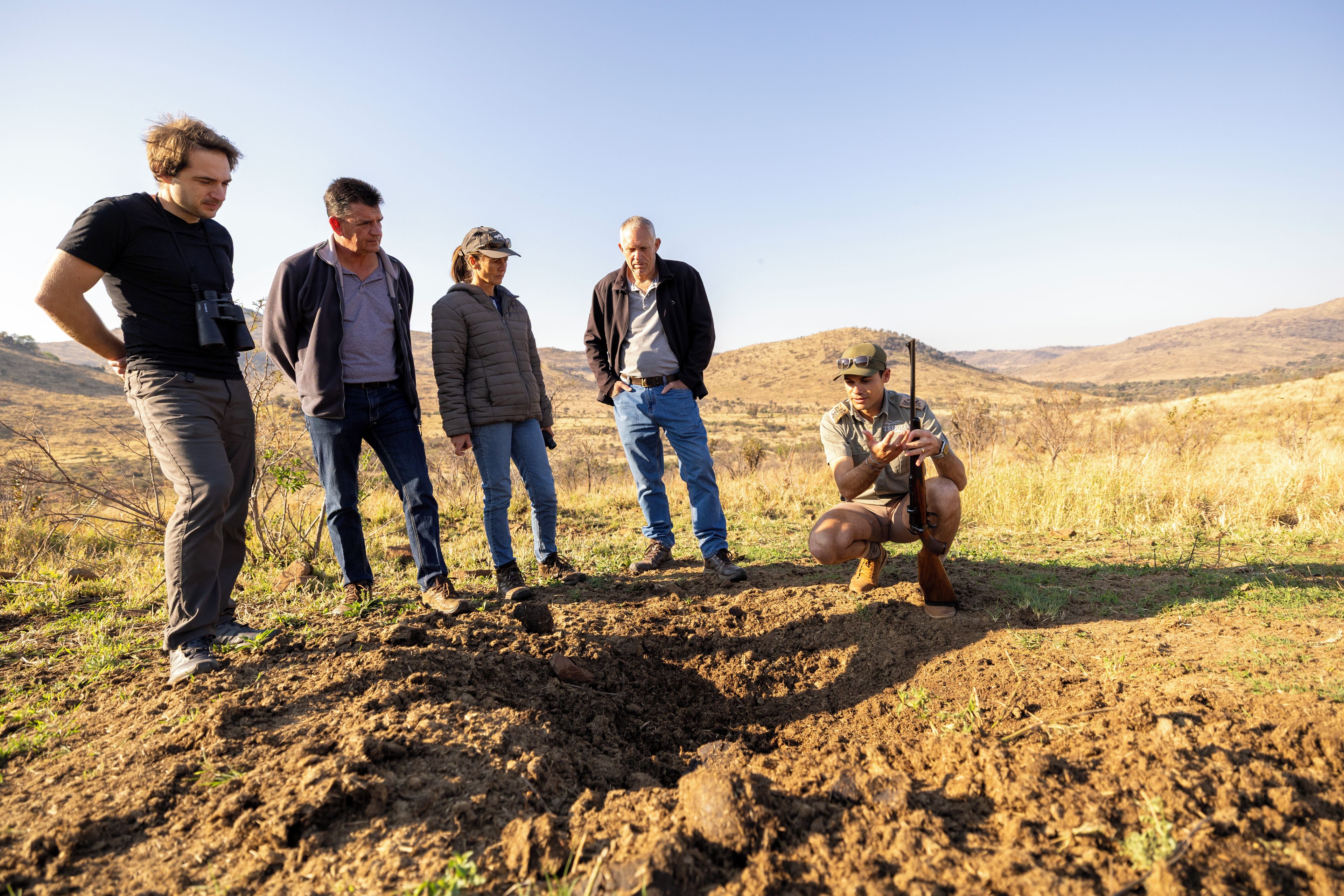A group of people in an outdoor setting with a hilly landscape in the background.