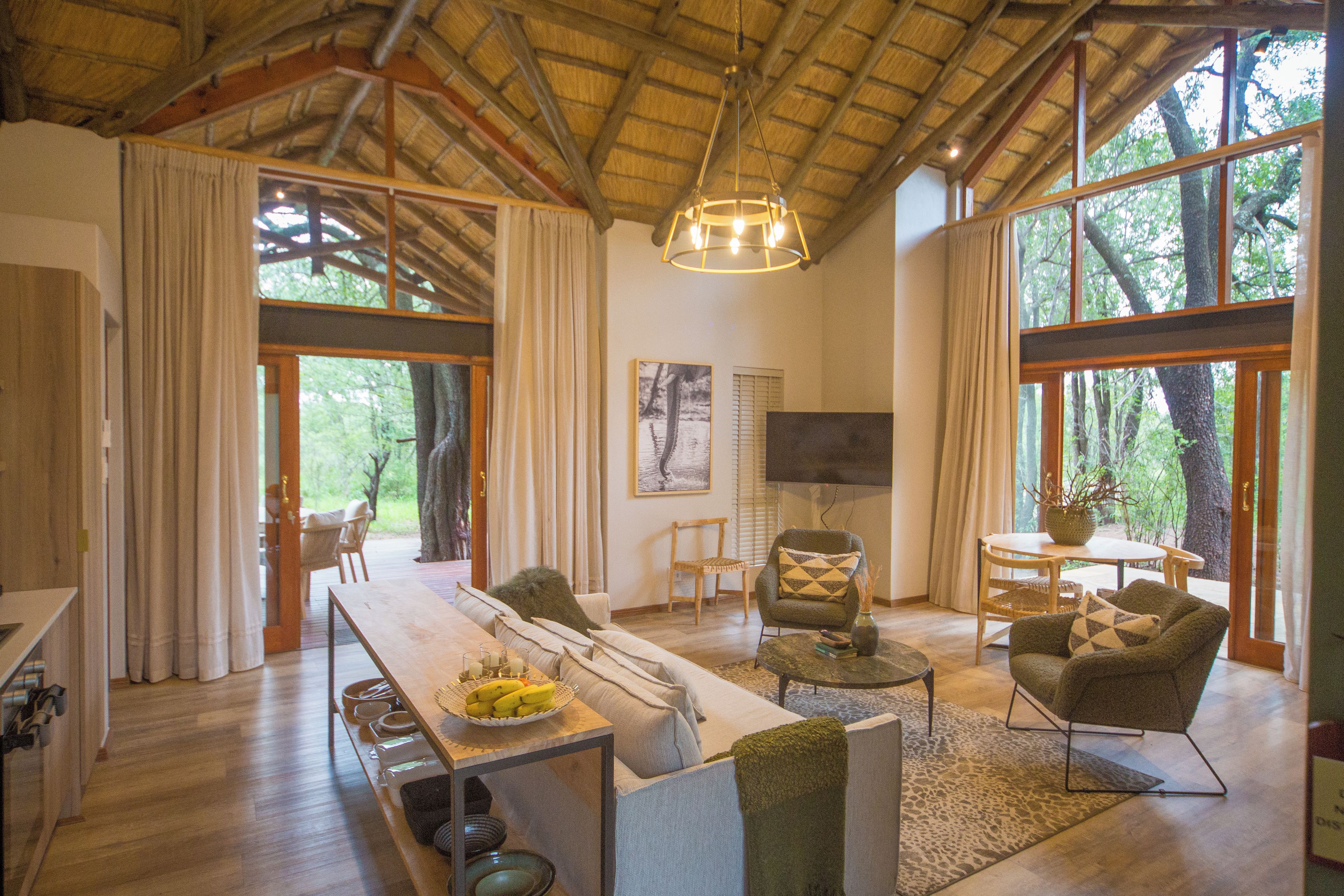 A spacious living area with a wooden ceiling, large windows, a dining table, and comfortable seating.