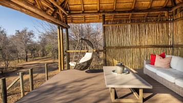 An outdoor seating area with a thatched roof, a hanging chair, a white table, and a sofa with red cushions.