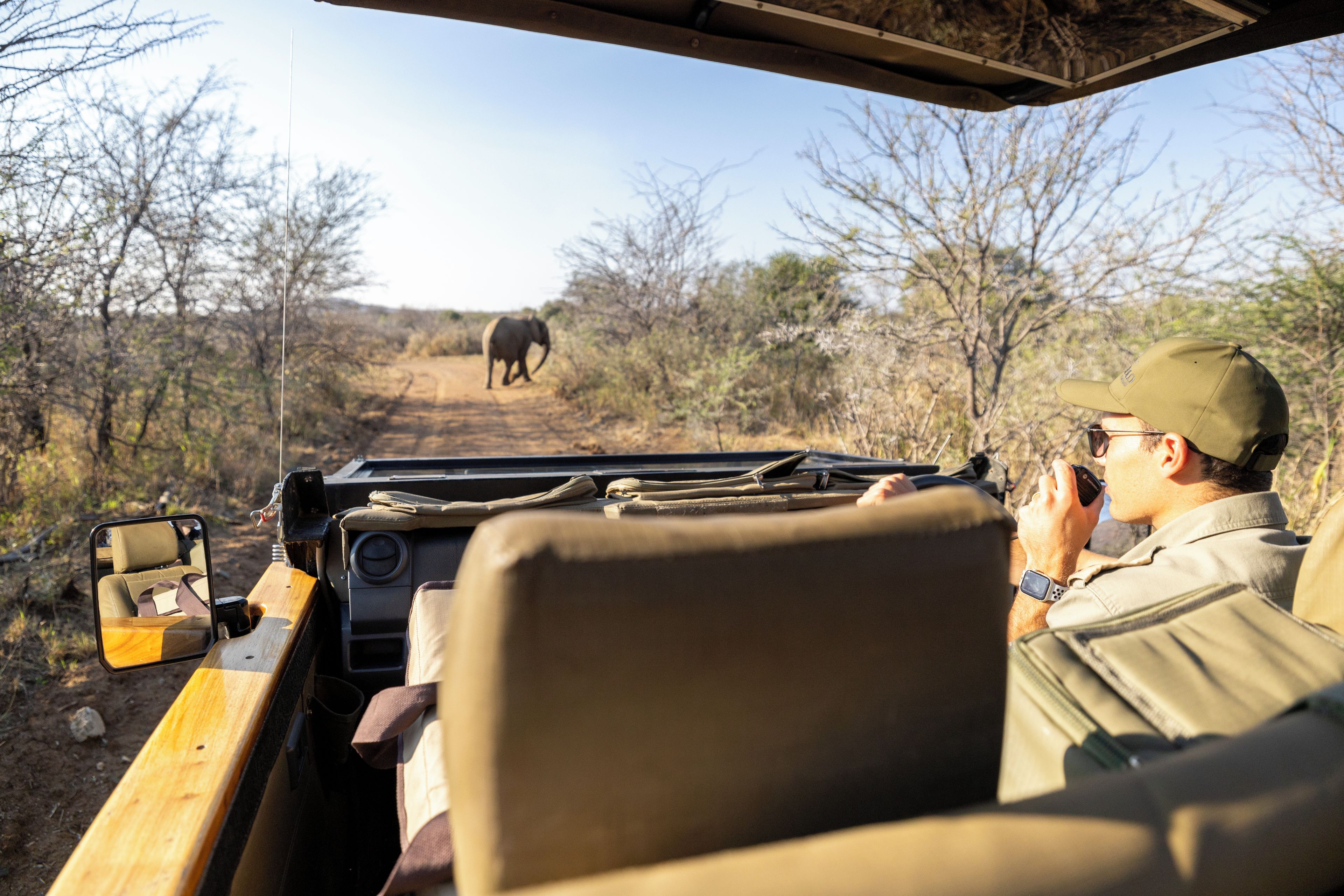 A safari vehicle interior with a person using binoculars, a map, and a GPS device.