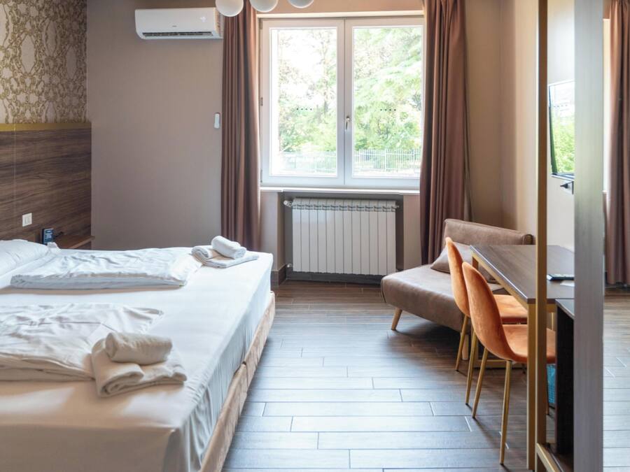Une chambre d’hôtel avec un lit, un bureau et une chaise, un radiateur et une fenêtre avec des rideaux.