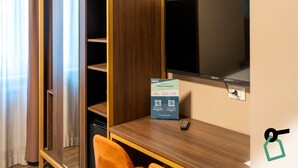 Une chambre d’hôtel avec un bureau en bois, un téléviseur fixé au mur et un panneau posé sur le bureau.
