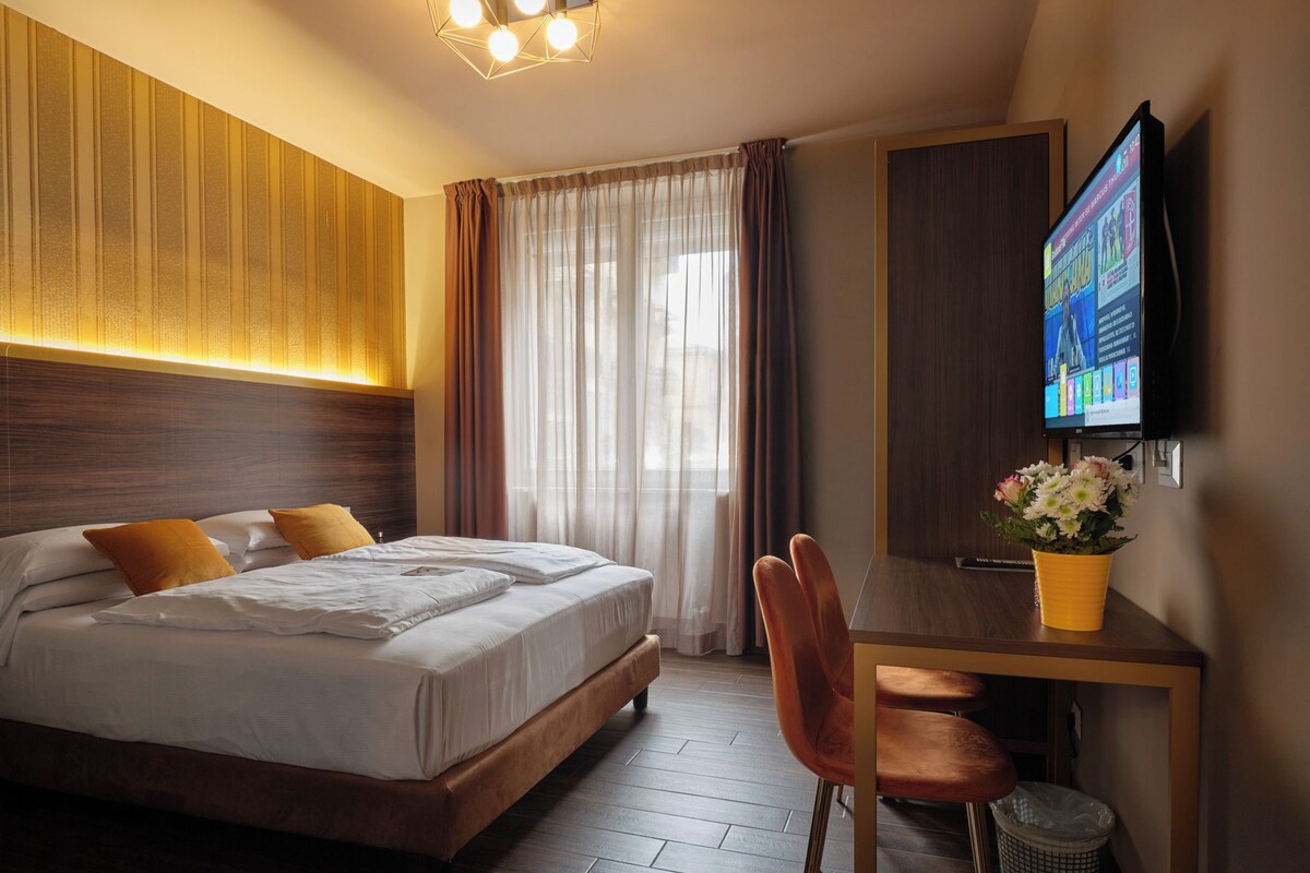 Une chambre d’hôtel équipée d’un lit, d’un bureau, d’une chaise, d’une télévision et d’une fenêtre avec des rideaux.