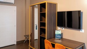 Une pièce de taille modeste, avec un bureau en bois, deux chaises orange, un téléviseur fixé au mur et une bibliothèque intégrée.