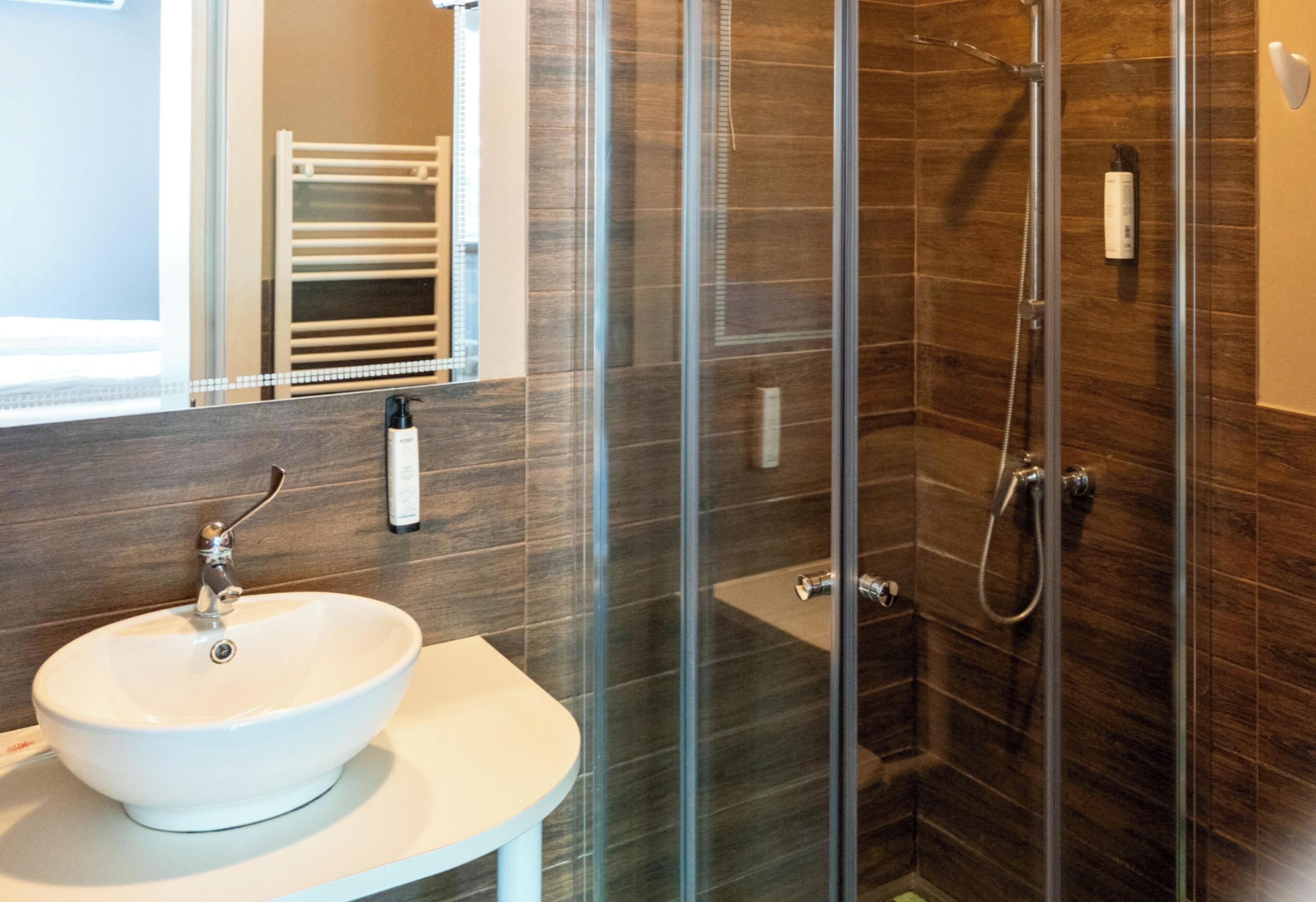 Un baño moderno con ducha de vidrio, lavamanos blanco y un perchero para toallas.