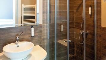 Un baño moderno con ducha de vidrio, lavamanos blanco y un perchero para toallas.
