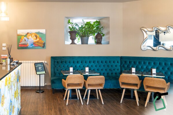 A restaurant with a teal upholstered booth, wooden chairs, and a painting on the wall.