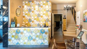 Un hall d’accueil d’hôtel avec un mur décoré de motifs, une horloge et un escalier menant aux étages supérieurs.