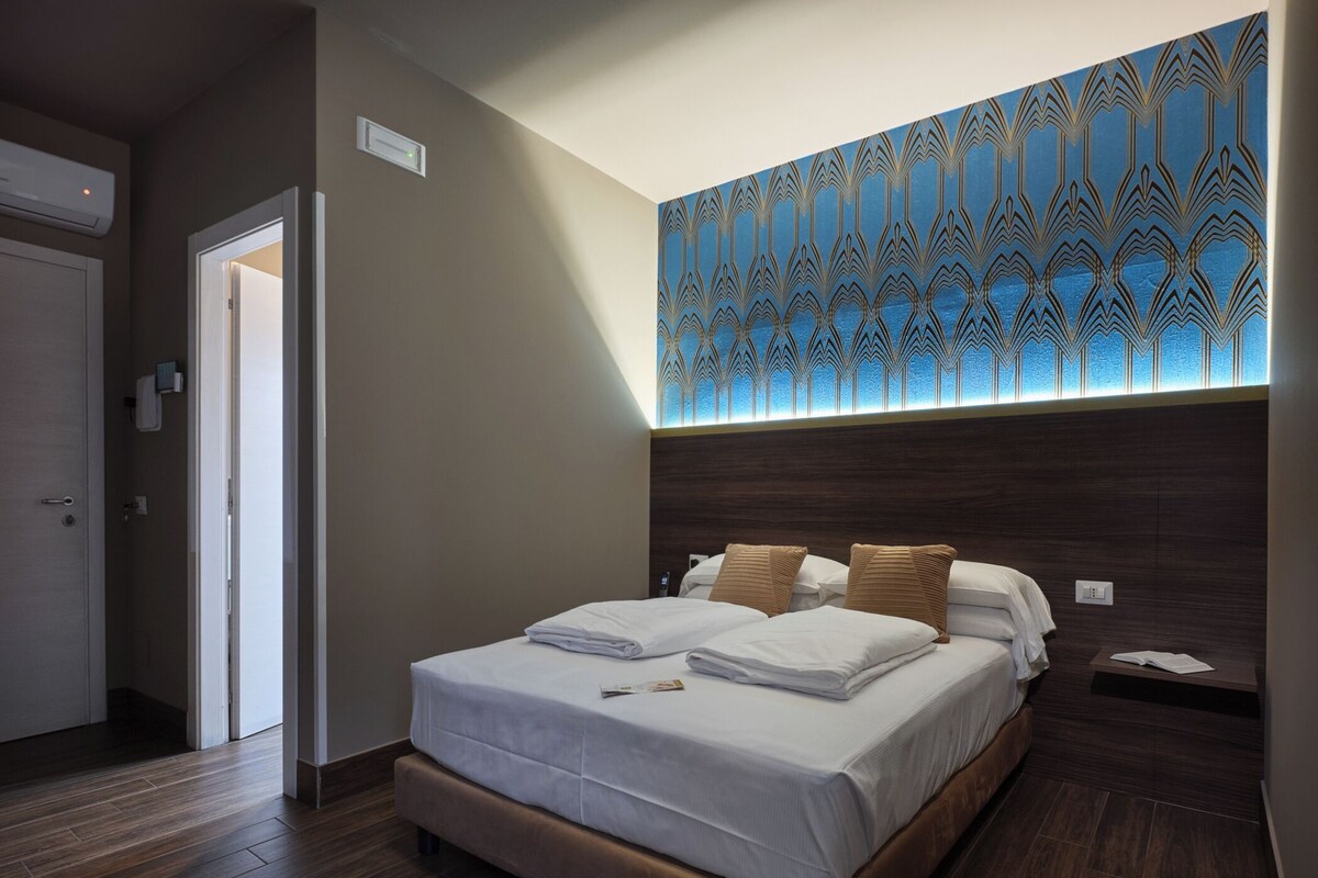 A hotel room with a bed, a nightstand, and a wall with a geometric pattern.